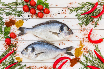 Fresh dorado fish, rosemary, cherry tomatoes, chilly pepper on white wooden table. Top view. 