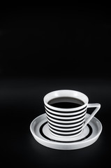 Hot drink in striped cup on the black background. Black and white minimalistic composition