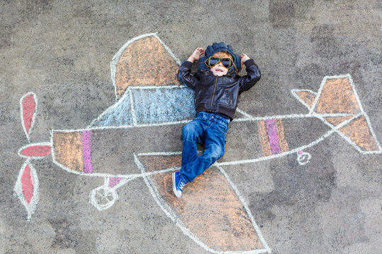 Little boy having fun with airplane picture drawing with chalk