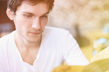 Fototapeta premium Young man reading a brochure. Toning, instagram effect. Blurred background. Looking at his side.