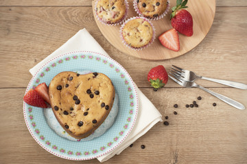 Heart shaped cake, served on blue plate with vintage roses. Chocolate covered strawberry Muffins. Strawberries and chocolate chips. Wooden table background.
