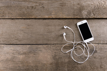 White cellphone with headphones on wooden background