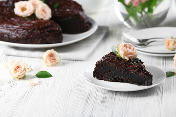 Piece of chocolate cake decorated with flowers on white wooden table