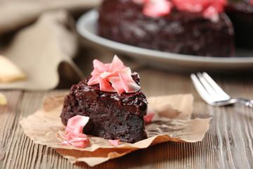 Piece of chocolate cake decorated with flowers on brown wooden table