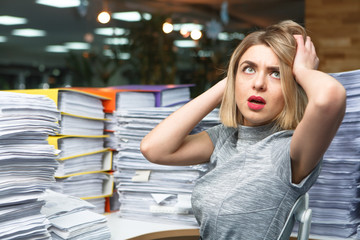 Office businesswoman at her desk full of documents, showing an overwhelmed expression