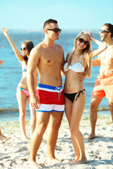 Happy couple and their playful friends relaxing at the beach, outdoors