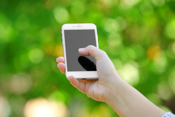 A female hand holding a mobile phone outdoors, on blurred background