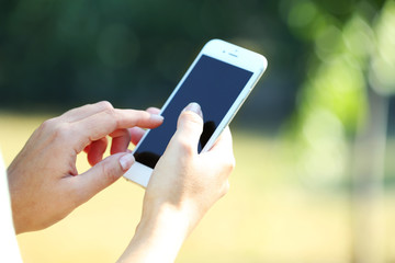 Female hands holding a mobile phone outdoors, on blurred background