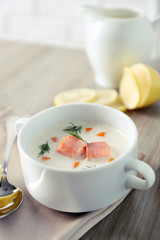 Delicious salmon cream soup on wooden table, which served with sliced lemon and spices