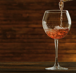 Rose wine pouring in glass on wooden background