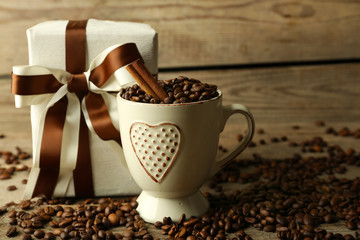 Beautiful gift with bow and coffee grains in mug, on wooden background