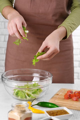 Female hands adding lettuce leaves into bowl with salad, close-up
