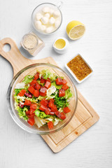 Tasty salad in glass dish on color wooden table background