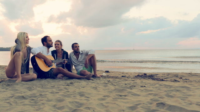 Couples have fun with guitar on beach at sunset