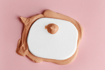 Makeup sponge with liquid foundation on pink background