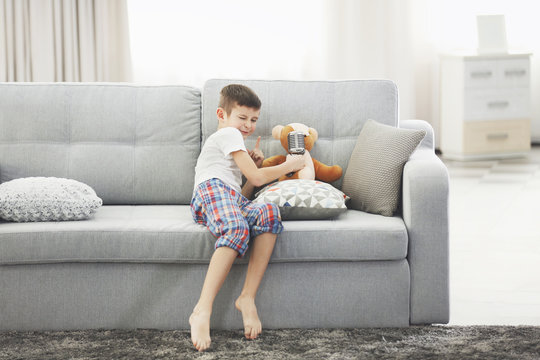 Little boy with Teddy bear singing with a microphone on a sofa at home