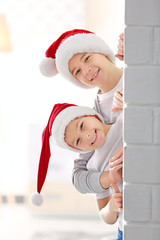 Brothers in Santa hats look out through a brick wall