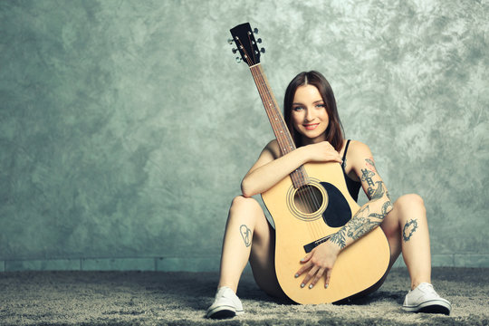 Woman with tattoo and guitar sitting on grey background