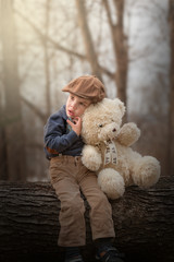 little boy sitting on a tree and hugging a teddy bear