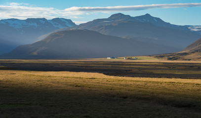 Beautiful scene when light touch yellow field and small farm with great mountain range background in Autumn season Iceland