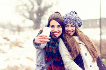 Two happy teenage girlfriends taking a selfie on snowy winter day