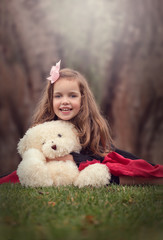 outdoor portrait of a beautiful dressed up girl holding a big teddy bear