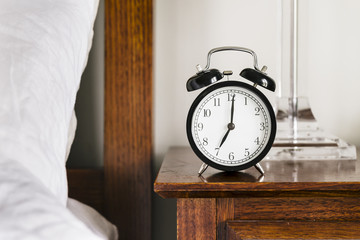 Black alarm clock showing 7 o'clock on bedside table
