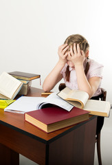 teenager girl sitting at a table in front of her large pile of books. schoolgirl reading a book and doing homework