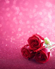 Three red roses over pink glittering background