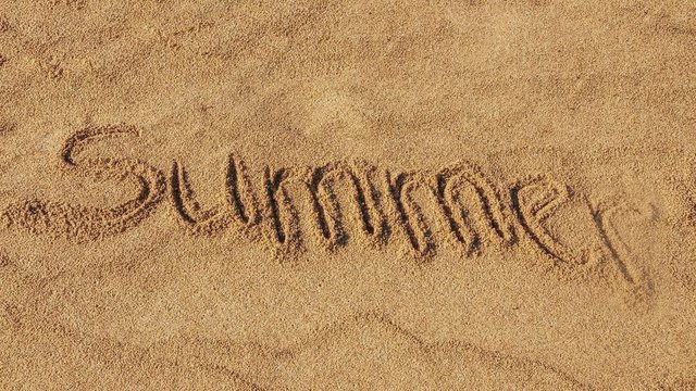 Word Summer appearing letter by letter on the sandy beach. Letters are handwritten.