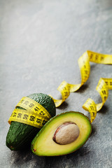 Avocado half and whole with tape measure on black background, diet concept
