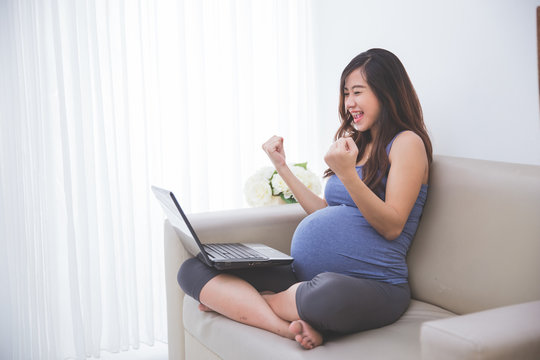 Beautiful pregnant asian woman sitting on the sofa with a laptop
