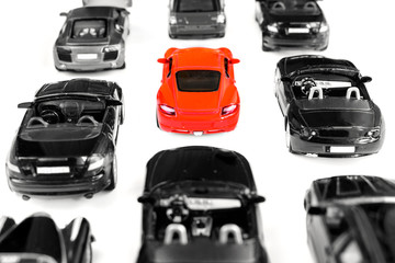 Red toy car standing out from crowd of plenty identical black car