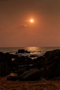 sun disk over sea at sunrise dark rocks on foreground