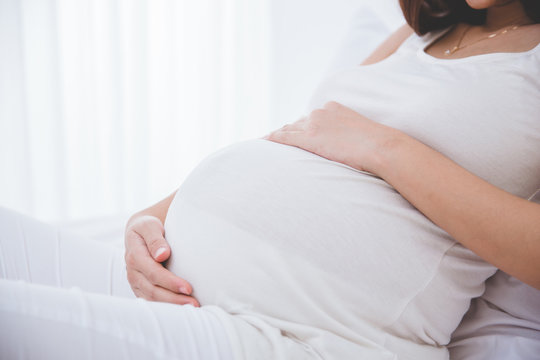 Pregnant woman leaning on the bed, close up on stomach