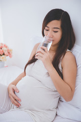 Beautiful pregnant asian woman holding a glass of water, smiling