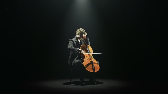 Cellist is tuning his cello alone on stage   