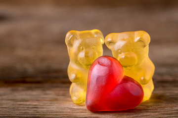 macro two yellow gummy bears with red hearts on wood