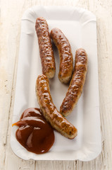 grilled sausages with ketchup on a square paper plate