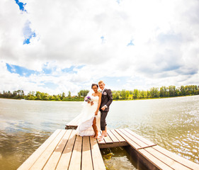 Beautiful bride with groom by a lake. Kiss and hug each other