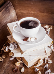 Cup of coffee, standing on the stack of old books. Wooden background
