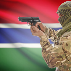 Fototapeta premium Male with gun in hands and national flag on background - Gambia