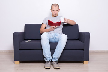 handsome man sitting on sofa with book and cup of tea