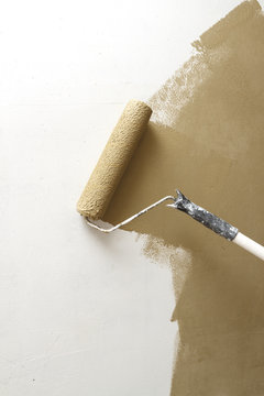 Paint roller applying paint on white wall, home improvements