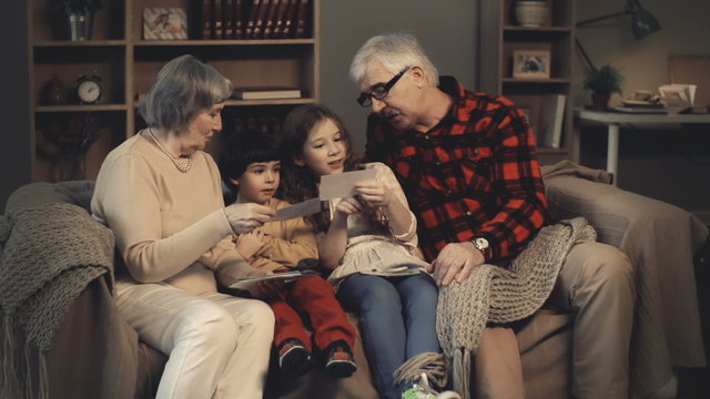 Senior couple and their grandchildren sitting on sofa and looking at family pictures 