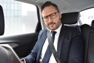 Businessman in taxi cab reading news on digital tablet