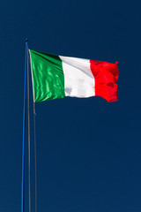 Large Italian flag waving in the wind against a dark blue sky