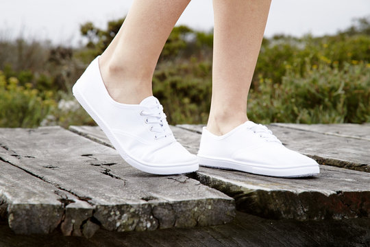 White sneakers on model walking on boardwalk, close up