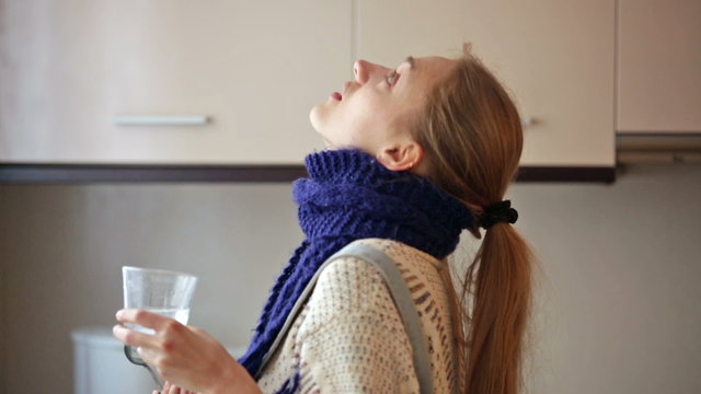 Girl with quinsy taking medicine and gargling throat in kitchen