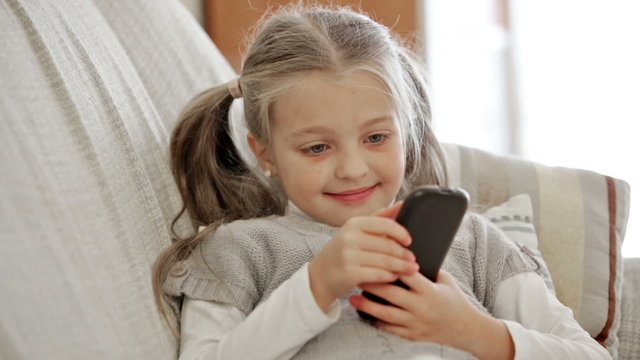 Cute little girl playing with smartphone at home